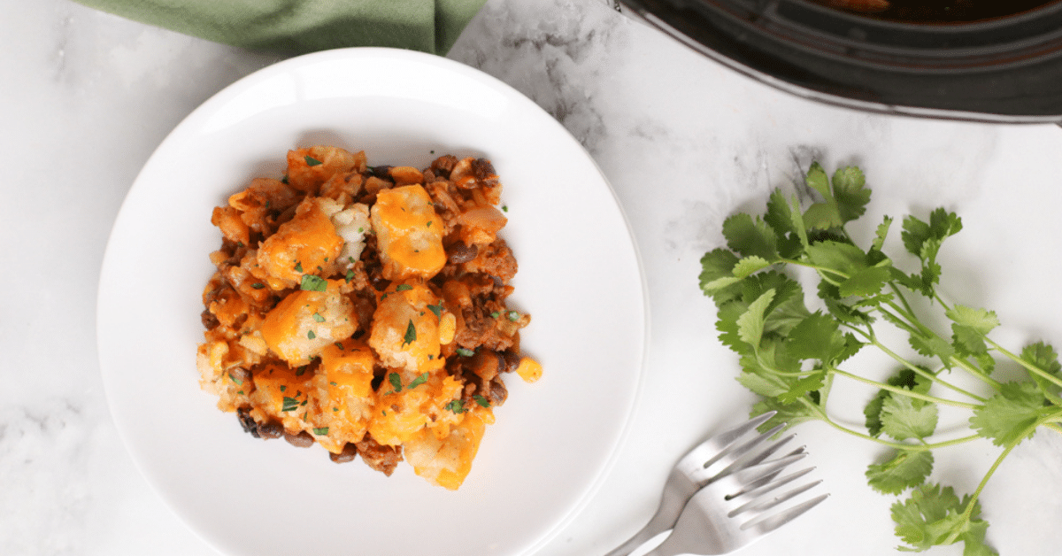 Tater tot casserole on shite plate with forks and cilantro on the side